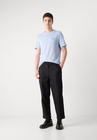 Lyseblå crew-neck t-shirt med lille sort logo, parret med sorte afslappede bukser og sorte snøre sko. Glat stof og enkelt design.
