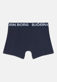 Bombažni bokserji v temno modri barvi, s belim elastičnim pasom z blagovno znamko. Oblika vključuje pravokotno obliko in ojačane šive.