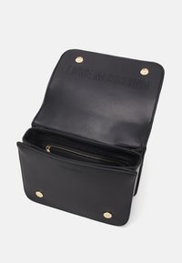 Svart läderbudväska med guldhardware. Har präglad "LOVE MOSCHINO"-logotyp och en fack med dragkedja inuti. Lockstängning.