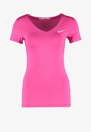 Femme portant un t-shirt rose Nike, un short noir avec un grand logo blanc Nike, et des chaussures de course noires et vert fluo, posant en marchant de côté.
