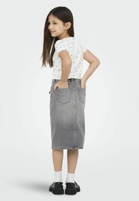 Balta trumpa rankovėmis marškiniai su juodomis taškeliais, derinami su pilka džinsine sijonu. Juodi batai su storais pažemiais. Modelis turi ilgus plaukus ir rankas kišenėse.