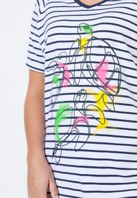 Krátký rukáv bílého trička s námořnickými vodorovnými pruhy. Obsahuje grafiku želv v černém obrysu s barevnými akcenty v zelené, růžové a žluté.