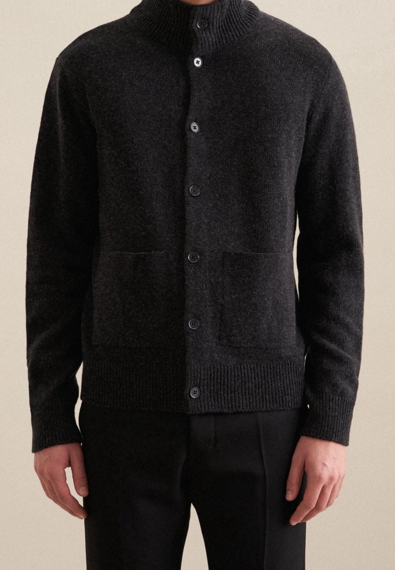 Tumma harmaa neuletakki neulotusta kankaasta, jossa on korkea kaulus, kuuden napin suljenta ja kaksi etutaskua. Resorit hihansuissa ja helmassa.