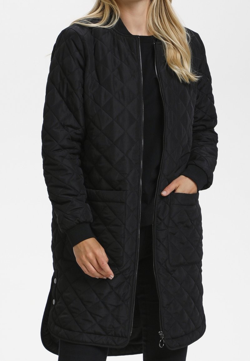 Schwarzer gesteppter langer Mantel mit einem Reißverschluss, gerippten Bündchen und seitlichen Taschen. Verfügt über ein Rautenmuster und kleine Metalldetails am Saum.