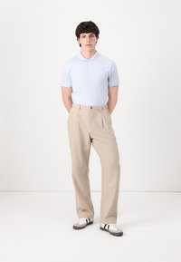 Light blue polo shirt, beige trousers, white sneakers with black stripes, standing pose, neutral background, smooth fabric texture.