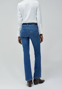 Niebieskie dżinsy flare, średnie zabarwienie, z dwoma tylnymi kieszeniami i wysokim stanem. W połączeniu z białą bluzką z długim rękawem.