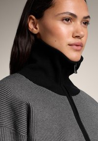 Czarny i szary sweter dziany z wysokim kołnierzem, z subtelnym wzorem pepitki i zamkiem błyskawicznym przy szyi.