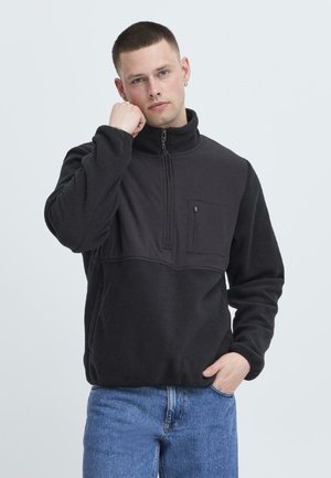 Black fleece pullover with a half-zip collar, featuring a chest pocket. The fabric has a soft texture and the design includes a contrasting panel.