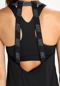 Takaa oleva näkymä henkilöstä, joka käyttää mustaa urheiluliiviä, jossa on mustat Nike-hihnat näkyvissä olkapäillä ja ilman hihoja olevassa paidassa.