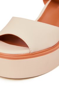 Ljust rosa plattformssandaletter med ett brett rem och öppen tådesign. Texturerad gummisula med ett orange accentband.