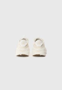 Sleek, cream-colored sneakers with textured fabric and a speckled sole. Features a pull tab at the heel and smooth, rounded design.