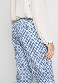 Pantalon bleu à motifs géométriques, avec une poche arrière et un tissu léger. La ceinture est positionnée à la taille naturelle.