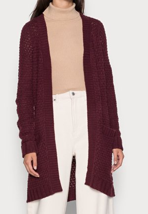 Bordeaux gebreide cardigan met open voorkant, ribgebreide randen, een textuurpatroon en twee voorzakken, gedragen over een beige coltrui.