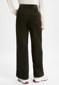 Groene corduroy wijde broek met een gestructureerde afwerking, voorzien van achterzakken en een hoge taille. Gekenmerkt door het dragen van witte en roze sneakers.