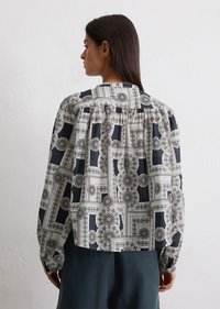 Losse blouse van een gemêleerde stof met geometrische designs in blauw, wit en groen. Lange mouwen en een geplooid detail aan de achterkant.