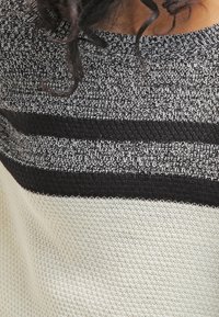 Pull en maille avec un col arrondi, présentant un motif rayé texturé noir et blanc sur une base crème claire.