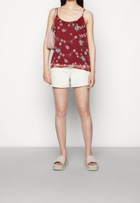 Top sin mangas de flores rojas con tirantes finos, combinado con pantalones cortos blancos y sandalias de plataforma beige. Un pequeño bolso rosa cuelga del hombro.