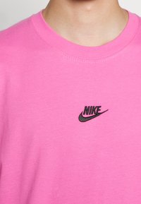 Lyserød bomuld t-shirt med rund halsudskæring. Har et lille sort Nike-logo på brystet. Glat tekstur, korte ærmer, afslappet design.
