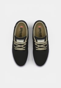Black sneakers with beige laces, canvas upper, round toe, and white rubber sole. Features logos on the tongue and side.