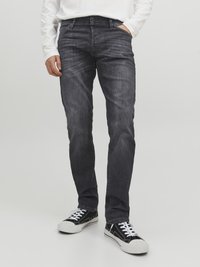 Pantalones vaqueros de mezclilla gris oscuro con un corte recto, diseño de cinco bolsillos y un ligero efecto desgastado; combinados con zapatillas de deporte en blanco y negro.