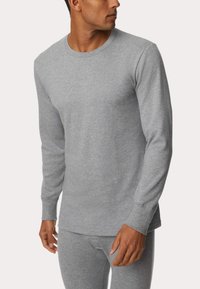 Maglia termica grigia a maniche lunghe realizzata in tessuto a coste, con scollatura a girocollo e maniche attillate, abbinata a pantaloni coordinati.