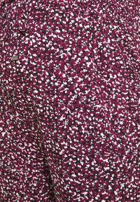 Close-up of fabric with an elastic waistband and drawstring featuring a dense maroon, white, and black abstract floral pattern.