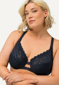 Seno navy blu con dettagli in pizzo lungo il bordo superiore, spalline regolabili e un design scallop. Dotato di una chiusura frontale con ganci.