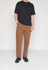 Camiseta negra de manga corta combinada con pantalones cargo marrones, con bolsillos y un ajuste relajado. Calzado: zapatillas deportivas negras.