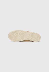 Semelle d'une basket Nike beige avec des motifs de bande circulaires et en grille, avec le logo Nike au niveau du médio-pied.
