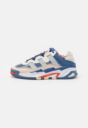Sneaker met een bovenwerk van mesh en suède in crème, blauw en rood. Voorzien van drie blauwe strepen, een dikke witte en blauwe zool, en contrasterende accenten.