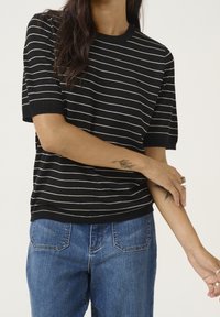 Sort kortærmet stribet sweater med cremede vandrette striber, med ribbet halsudskæring og kant, parret med lyseblå denim jeans.