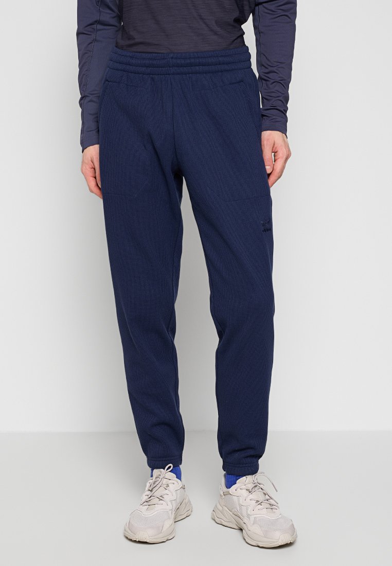 Marineblauwe sportbroek van textiel met een elastische tailleband, zijzakken en subtiele branding op het been.