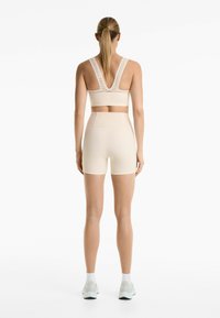 Beige sportbeha met brede bandjes, met een open rugontwerp en geperforeerde details, gecombineerd met hoge beige shorts.