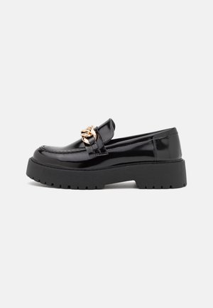 Black patent leather loafers with a chunky black sole and gold hardware detailing. Smooth texture and rounded toe design.