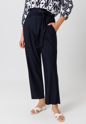 Marineblauwe wijde broek met hoge taille, stoffen riem, zijzakken en een gladde textuur, gecombineerd met witte sandalen met bandjes.