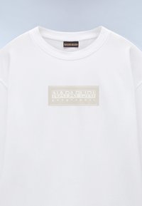 Valkoinen puuvillaneule, jossa on suorakulmainen vaalea logopatchi, jossa lukee "NAPAPIJRI geographic" etupuolella. Pyöreä kaula-aukko.