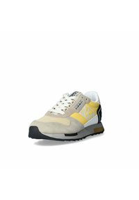 La sneaker presenta una toma superiore in scamosciato beige con dettagli in rete gialla. Suola in gomma nera e controtallone bianco. Lacci in tonalità neutra.