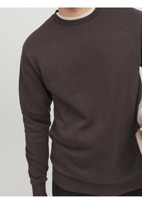 Felpa marrone scuro realizzata in misto cotone, con collo rotondo a coste e maniche lunghe. Morbido al tatto con una vestibilità rilassata.
