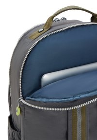 Zaino grigio con parte superiore arrotondata, dotato di un compartimento imbottito blu per laptop, messo in risalto da una maniglia e una cerniera verdi a contrasto.