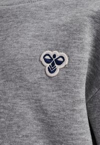 Grå sweatshirt-tyg med en mjuk textur, försedd med en vit och marinblå broderad bi-logotyp på vänster bröstområde.