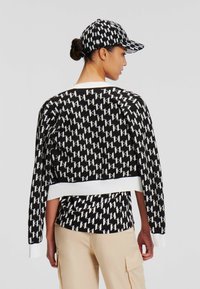 Maglione corto a righe in bianco e nero con maniche lunghe, orlo a coste bianco, indossato sopra un top coordinato, abbinato a pantaloni cargo beige.