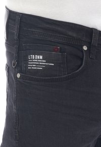 Svarta denimjeans med en klassisk design, femficks-layout och metallbeslag. Etiketten säger "LTB DNM, 100% handgjord."