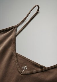 Braunfarbener Trägershirt mit verstellbaren Trägern, V-Ausschnitt und genähten Kanten. Beinhaltet ein Etikett mit der Aufschrift "THE SET" in der Nähe des Ausschnitts.