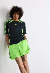 Tricou sport negru cu accente neon verzi și mâneci în dungi, asortat cu pantaloni scurți neon verzi; ambele din material ușor.