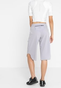 Shorts deportivos grises hechos de material ligero, con un bolsillo trasero y aberturas en el dobladillo, combinados con un top corto blanco y zapatos negros.
