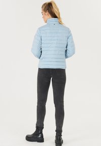 Lyseblå pufferjakke med høj krave, prydet med vandrette kviltede linjer og en tætsiddende silhuet, parret med sorte skinny jeans og støvler.