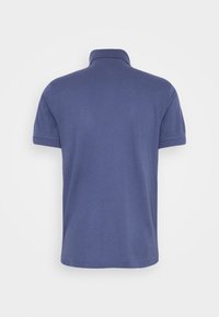 Blå kortärmad polo med ribbad krage, sedd bakifrån mot en helt vit bakgrund.