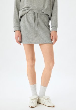 Graues Sweatshirtkleid mit Kordelzug in der Taille, lässiger Schnitt, weicher Stoff; kombiniert mit weißen Turnschuhen und gerippten weißen Socken.