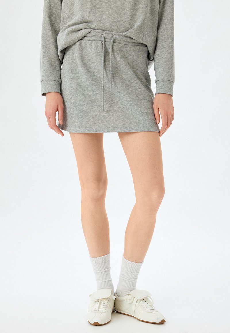Vestido sudadera gris con cintura ajustable, corte casual, textura suave; combinado con zapatillas blancas y calcetines blancos acanalados.