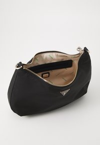 Clutch bag nera in nylon con hardware dorato, chiusura con zip e interno beige caratterizzato da un motivo con logo "GUESS". Include una tasca interna.
